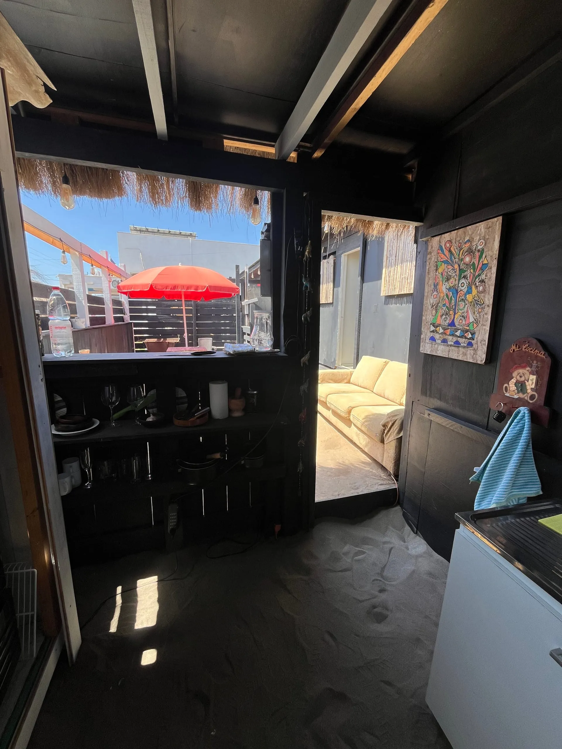 Cocina de la tiny house abierta al patio con quitasol y al sofá